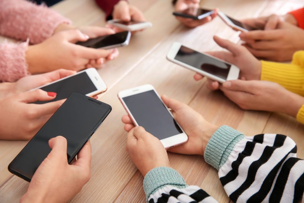 Young people using mobile phones on wooden table, close-up.