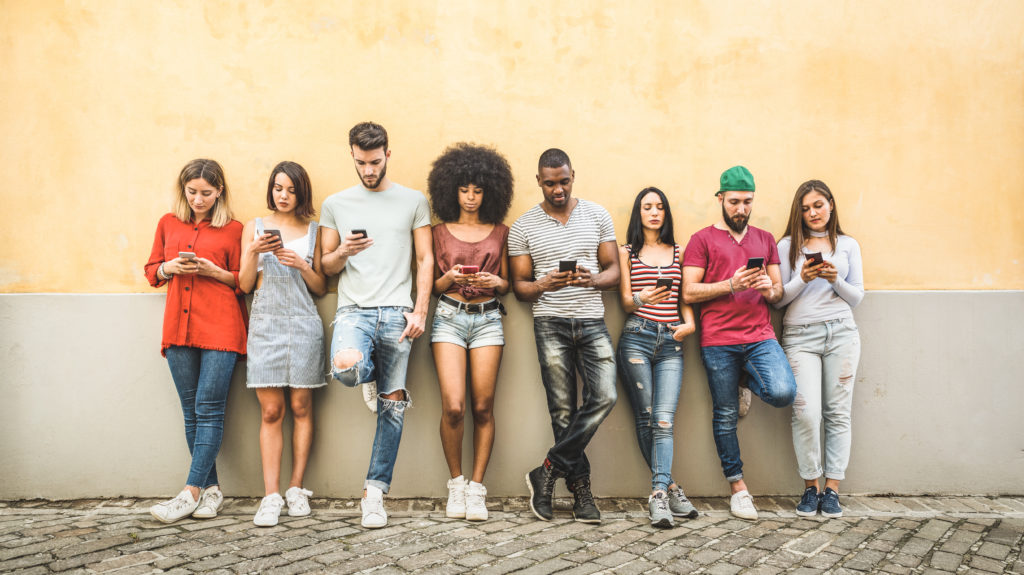Multiracial friends using smartphone against wall at university college backyard - Young people addicted by mobile smart phone - Technology concept with always connected millennials.