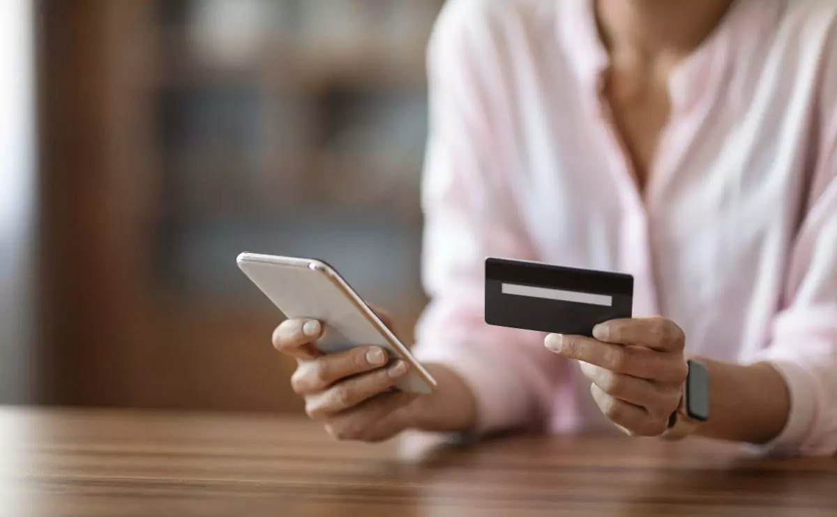 Female face not shown and with one hand holding her smart phone while another is holding a credit card
