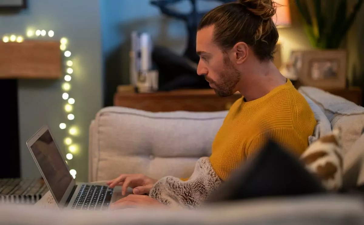 Man with a bun using his laptop while sitting on a couch 