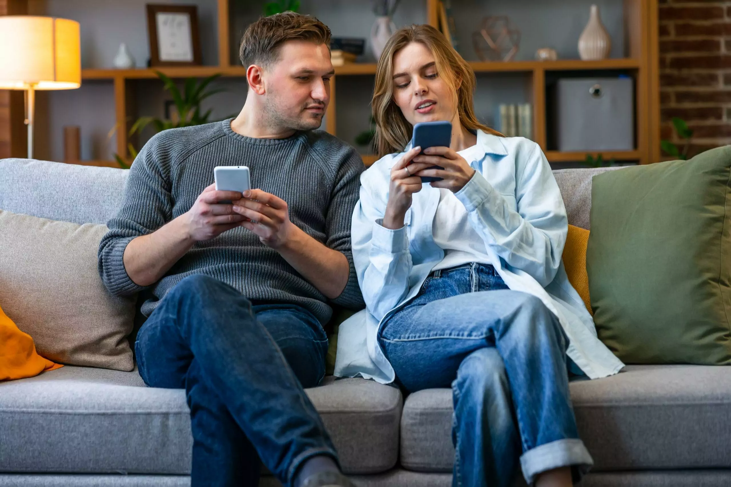 Young couple sitting on sofa holding smart phones