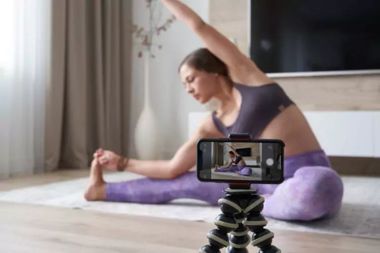 Young female blogger recording sports video at home doing yoga in living room