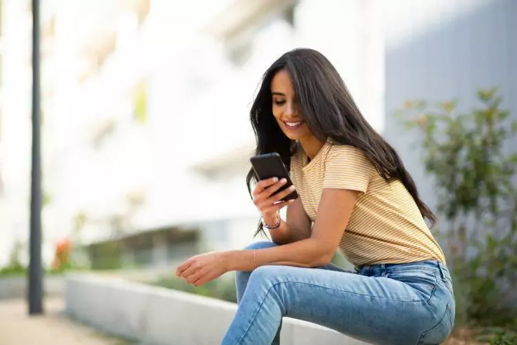 Young smiling woman sitting outside looking at mobile phone