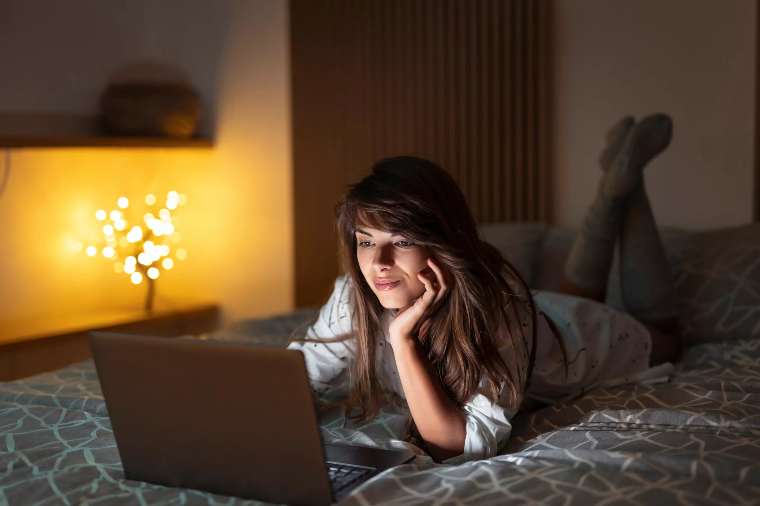 attractive young woman using her laptop while lying in bed