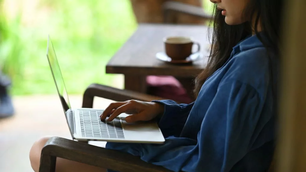 Young woman using a computer laptop while sitting at a wooden chair.