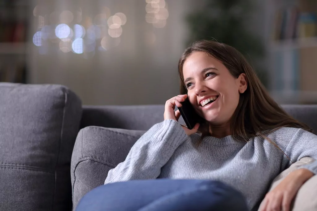 Happy woman talking on phone on a couch.