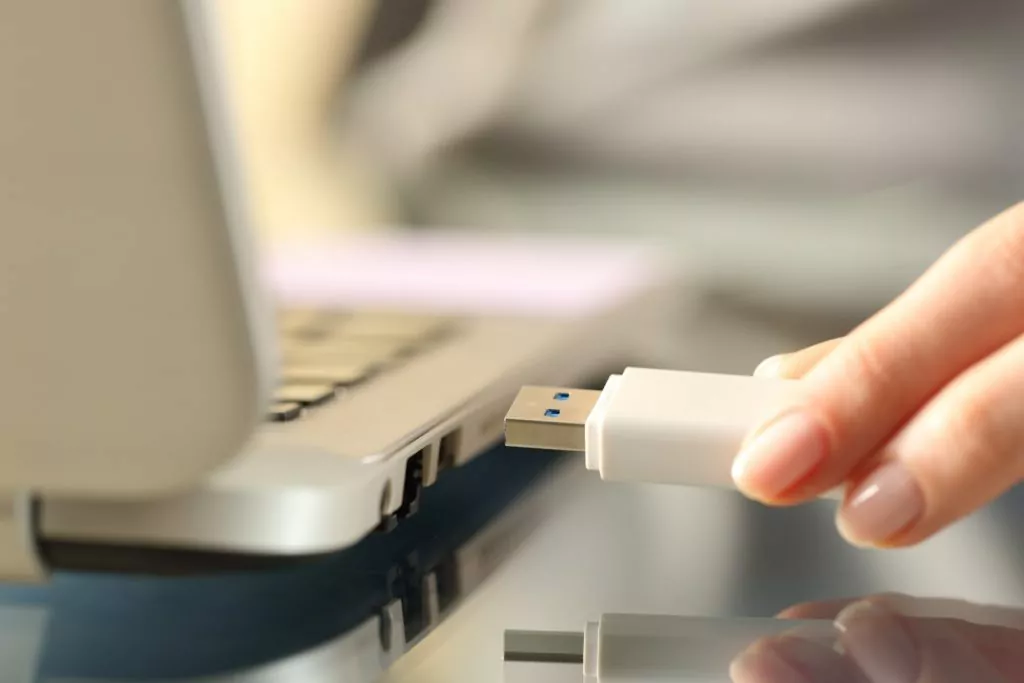 Woman connecting white USB flash drive to a laptop.