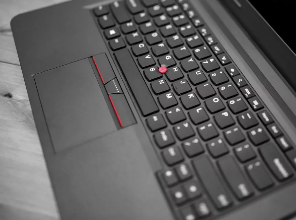 Black laptop keyboard trackpoint red dot cap and touchpad with button.