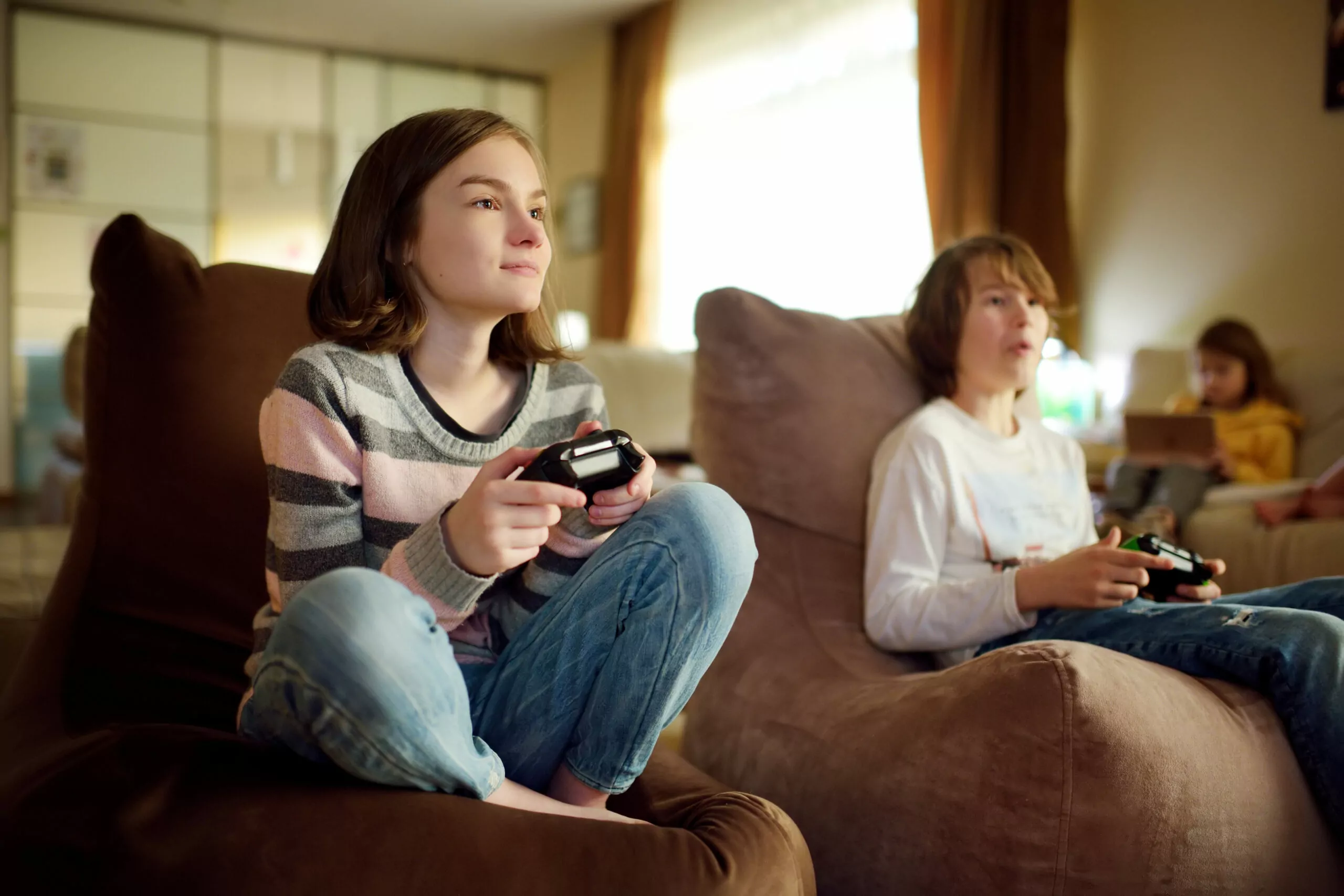 A group of preteen kids playing video games at home. Children sitting on the couch together holding gaming controllers.