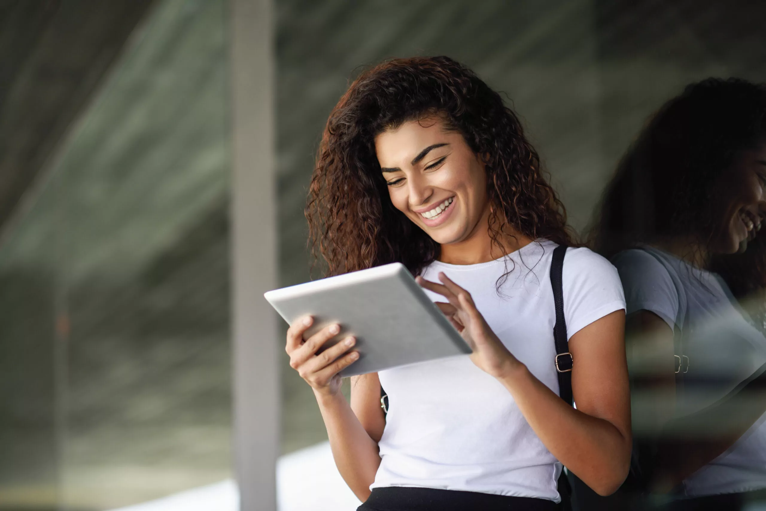 smiling beautiful woman using digital tablet outside the building