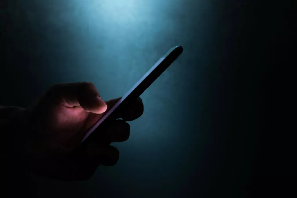 silhouette of hand holding and touching a mobile phone screen in the dark.