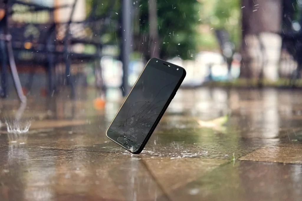 Smartphone falling and crashing on wet ground in the city park.