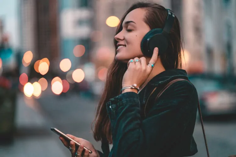 Young happy stylish woman teenager listening to music on phone via headset, outdoor
