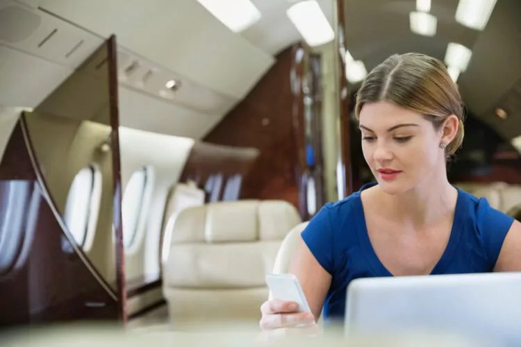 Young businesswoman using smartphone on airplane, trying to see if she can still view Snapchats messages.
