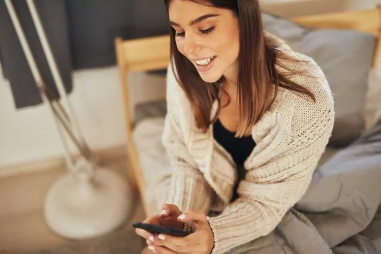 attractive brunette dressed in beige sweater using phone at home