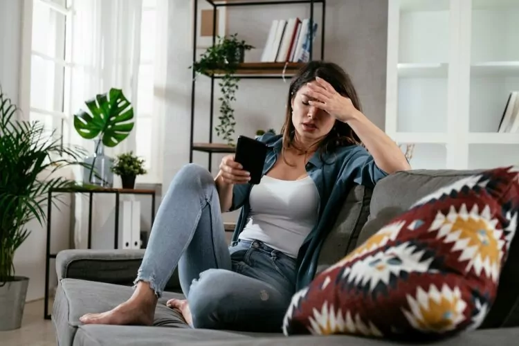 Sad woman sitting on the couch, using the phone.