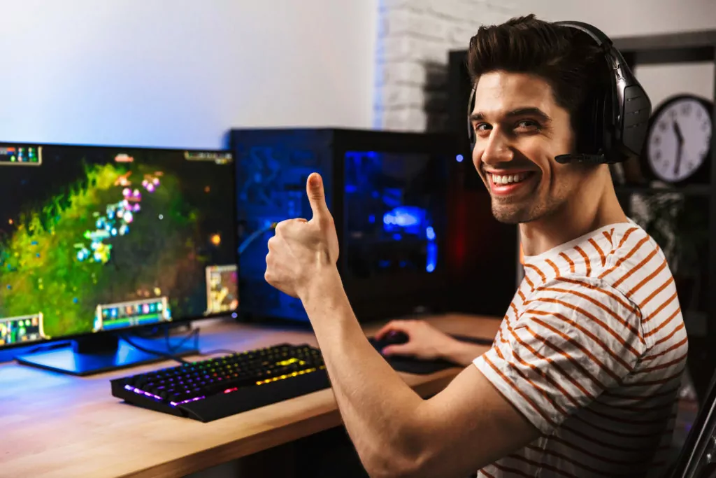 Joyful gamer guy with his thumbs up, playing video games on his computer.