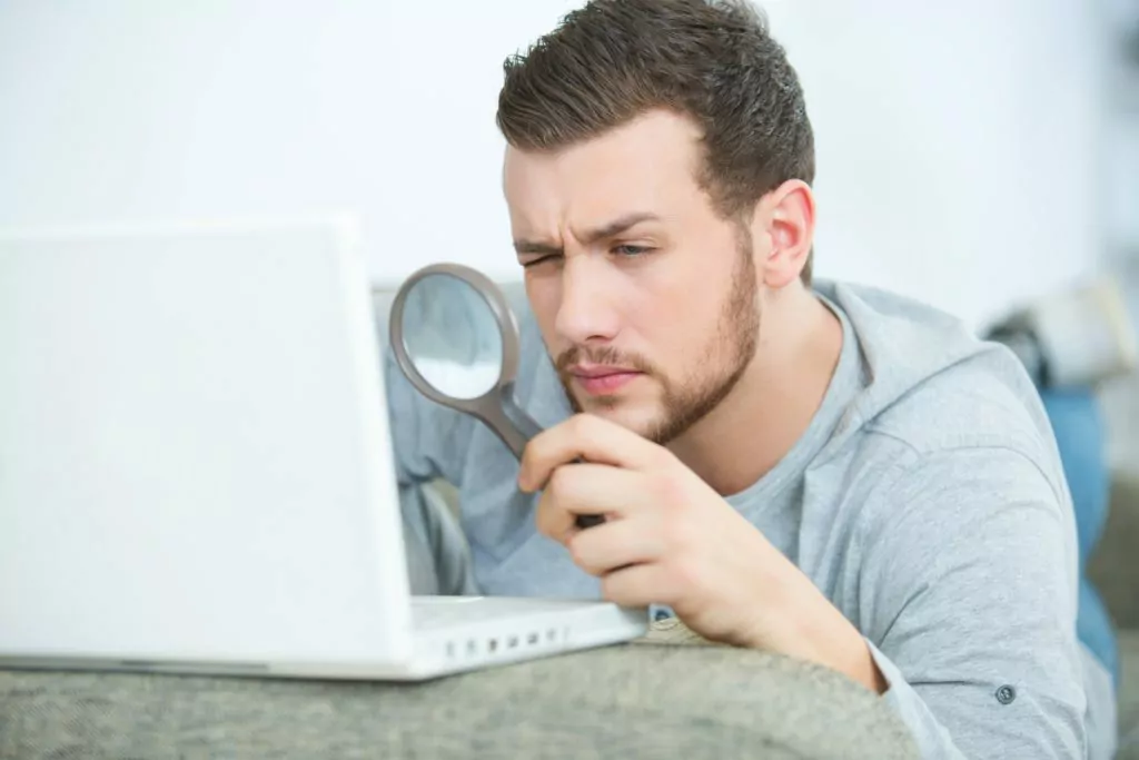 Man looking through a magnifying glass to his laptop.