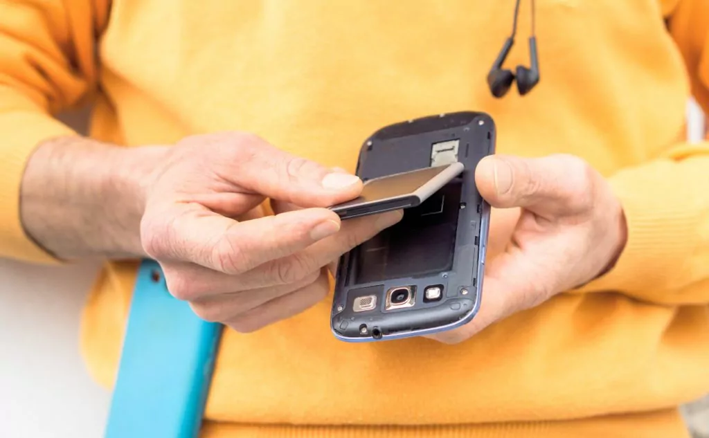 Man in orange shirt placing battery on a phone.