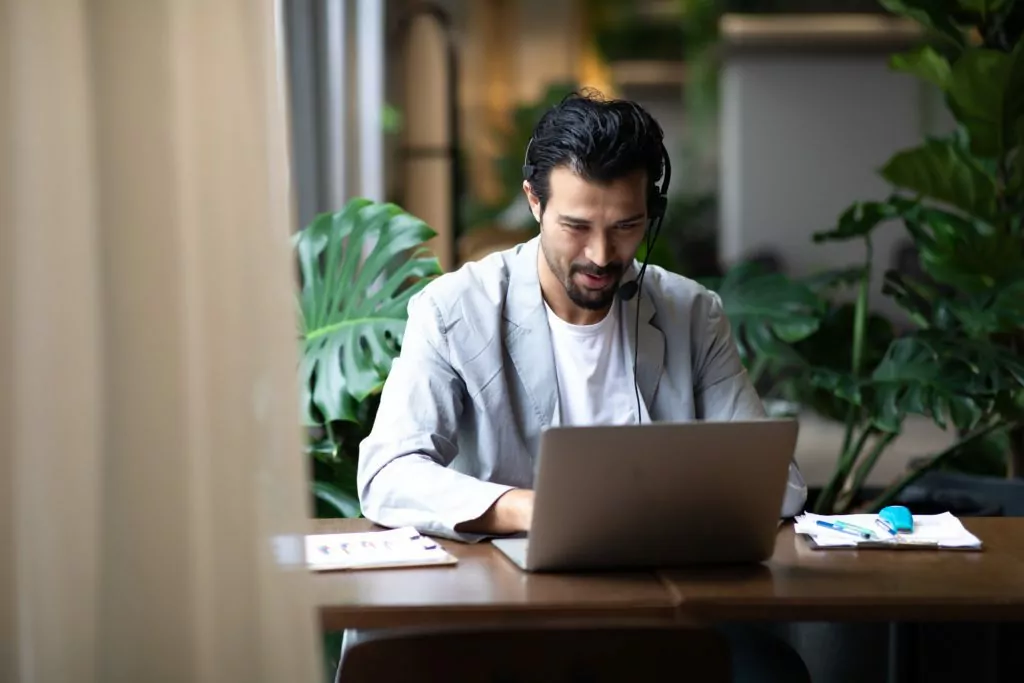 Man in suits and headsets smiling while working with his laptop inside modern office.