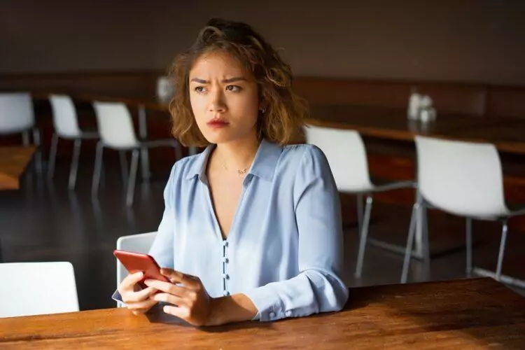 frowning woman holding phone looking away at cafe