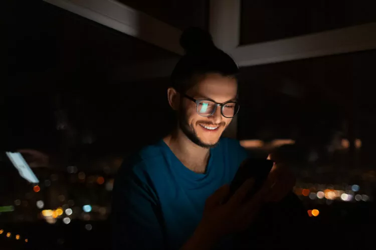 devious looking smiling man looking in smartphone in dark room at night