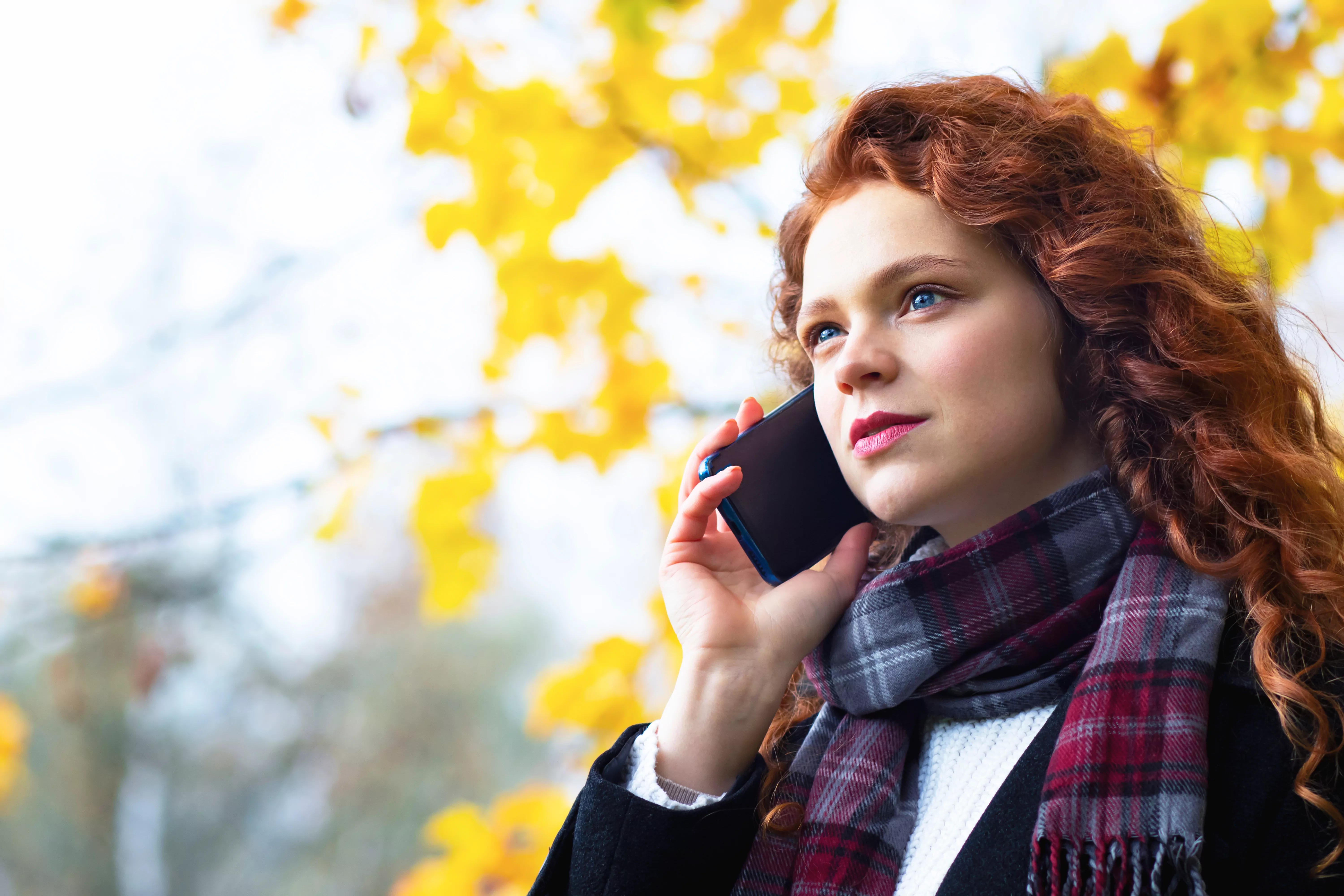 Serious woman speaks by mobile phone in the park outdoors in autumn. 