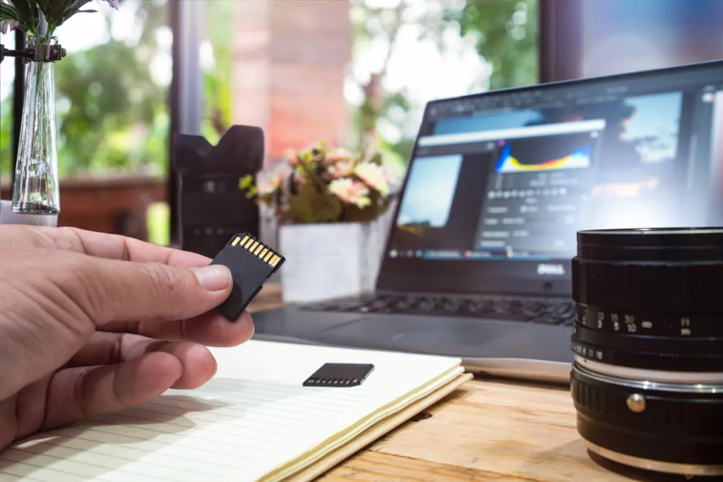 male hand holding a memory card in front of the laptop.