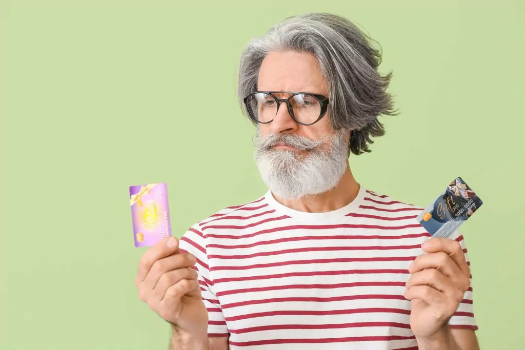 Senior man holding two gift cards, green background.
