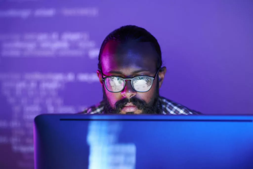 Serious programmer coding on computer with purple background.