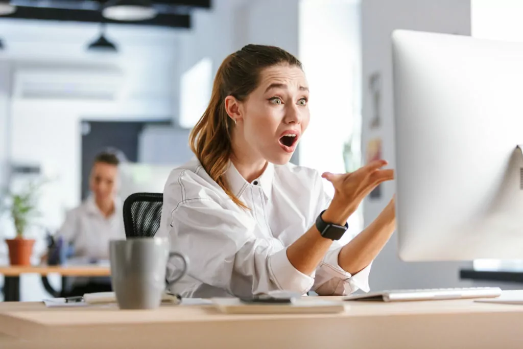Shocked woman in front of computer, inside workplace.