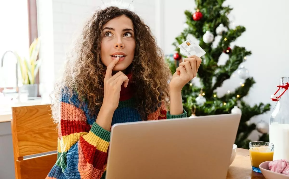 Woman in deep thought as she holds her credit card with the laptop open in front of her