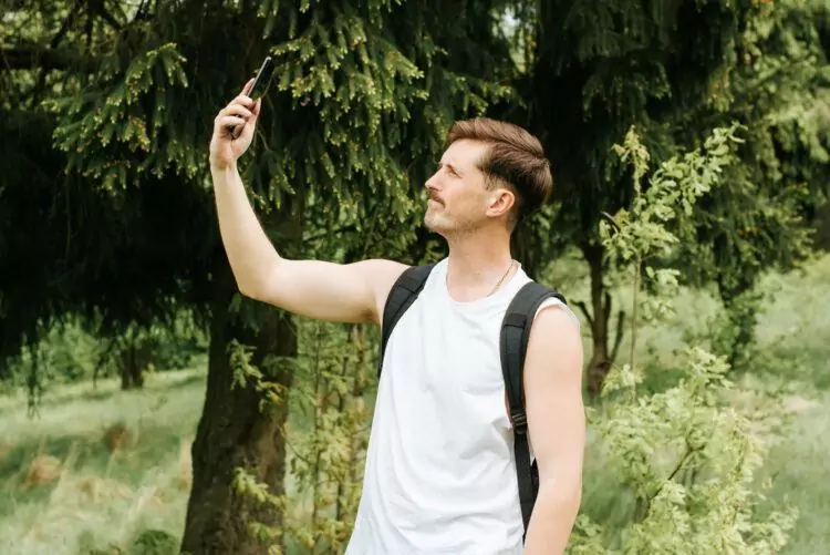 Man trying to catch signal on mobile phone outdoors in the forest. 