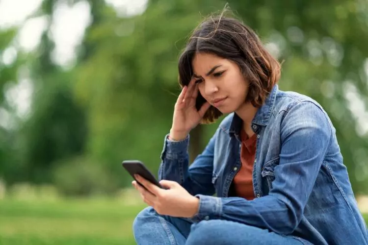 Worried young female reading a message on mobile phone while sitting outdoors