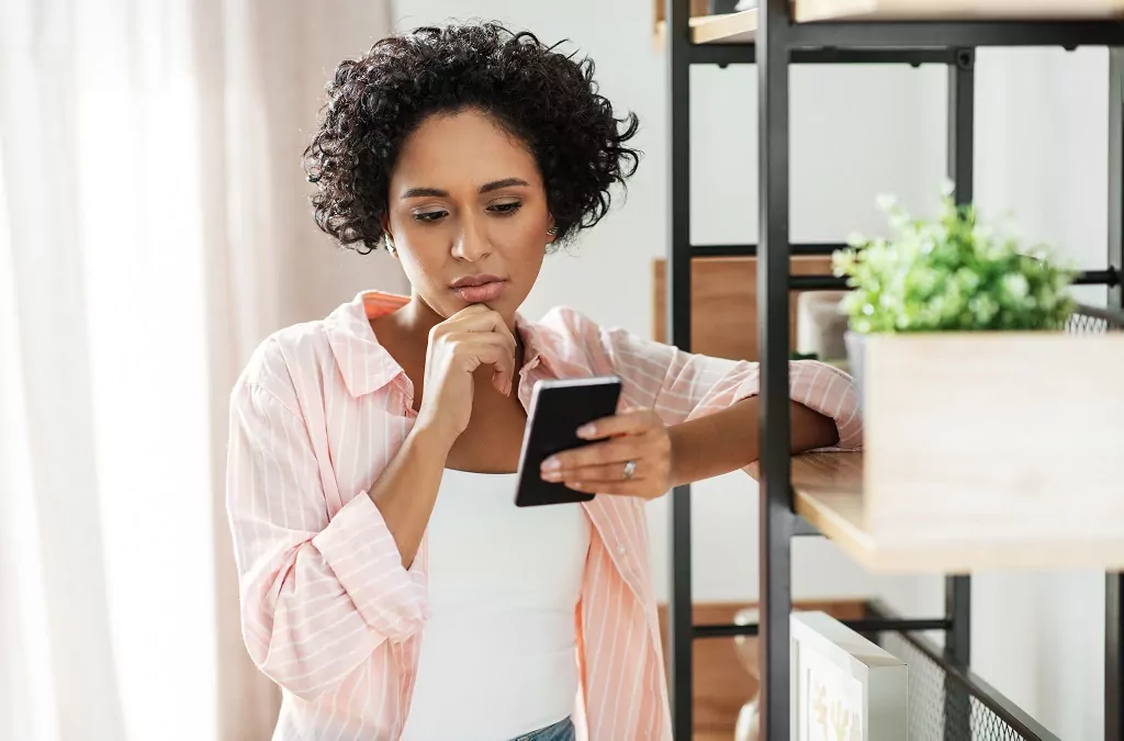Woman with smartphone looking suspicious and thinking at home.