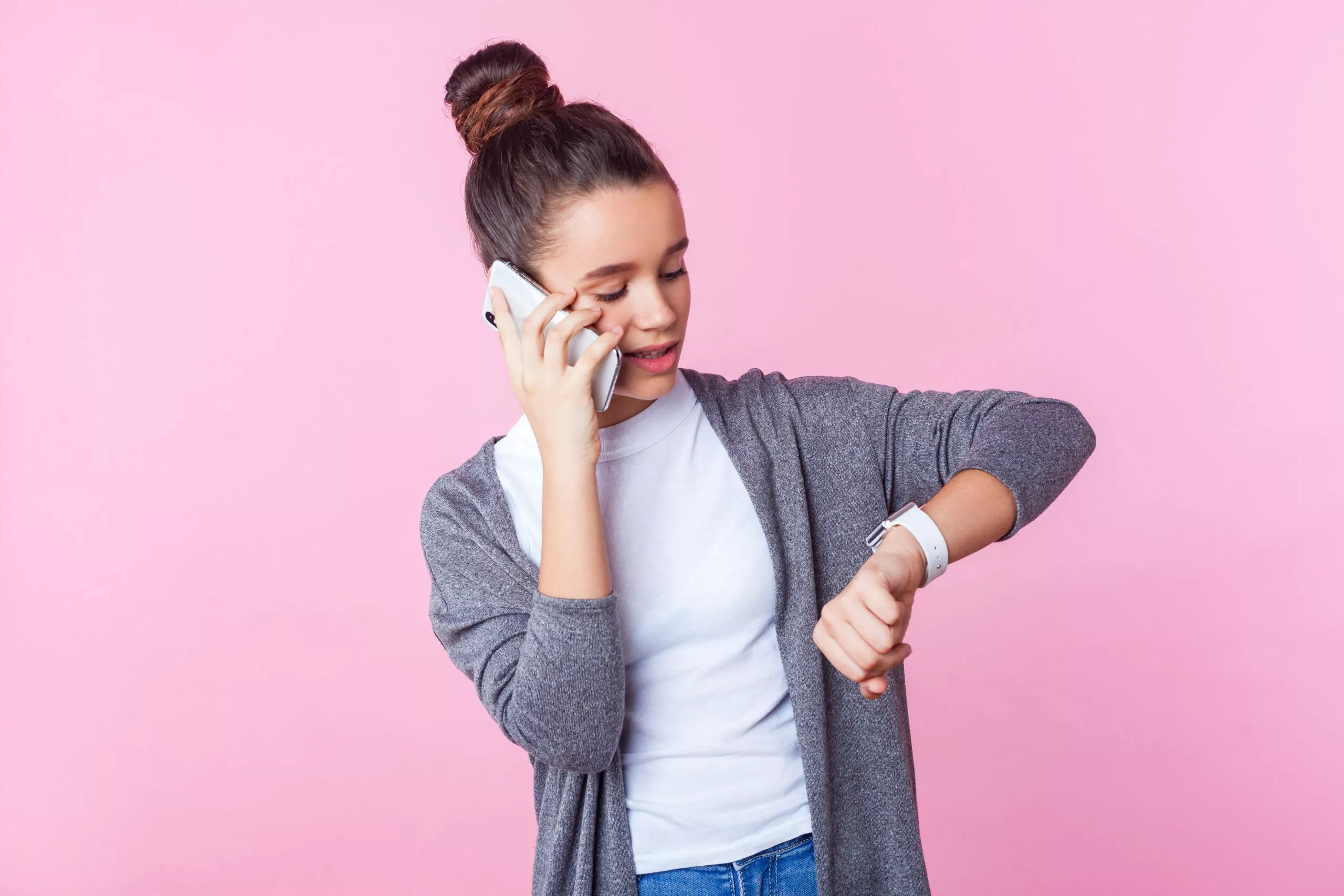Teenager looking at her watch while talking on the phone, pink background.