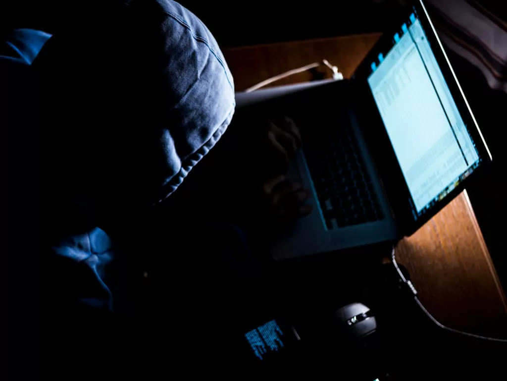 Man wearing a hoodie and using a computer in the dark.