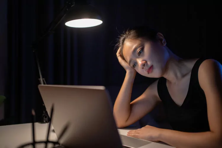 young asian woman looks tired stares at laptop screen