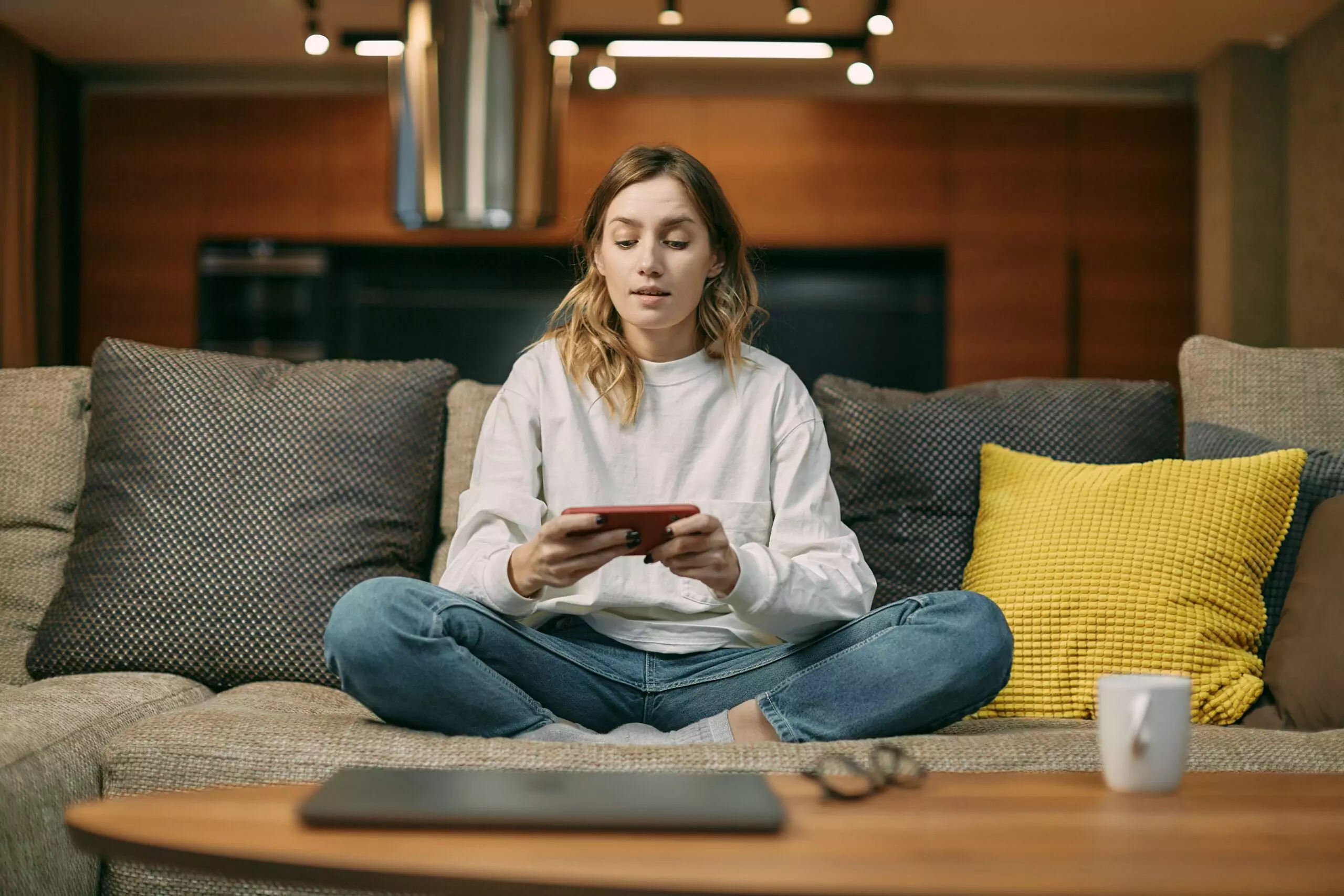 Female gamer playing mobile online game on smart phone with friends online sitting on sofa at home living room