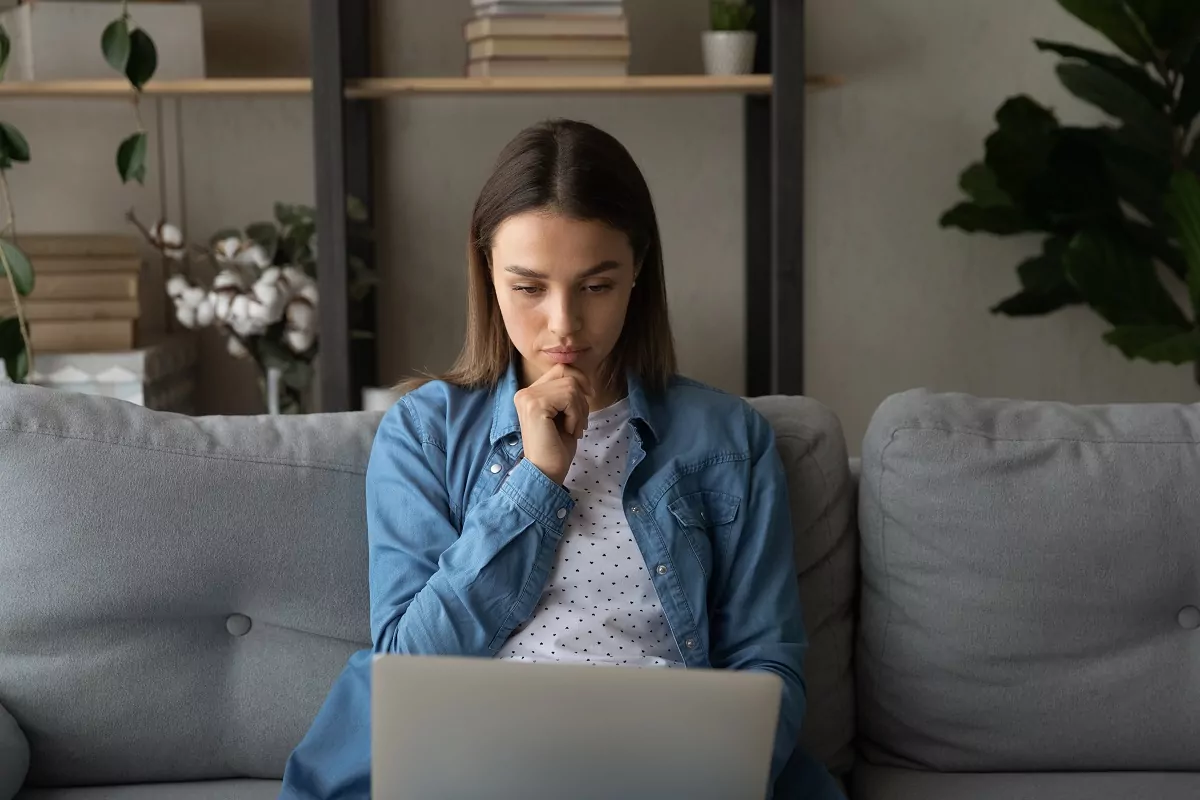 thoughtful woman sitting on the sofa looking at laptop screen 