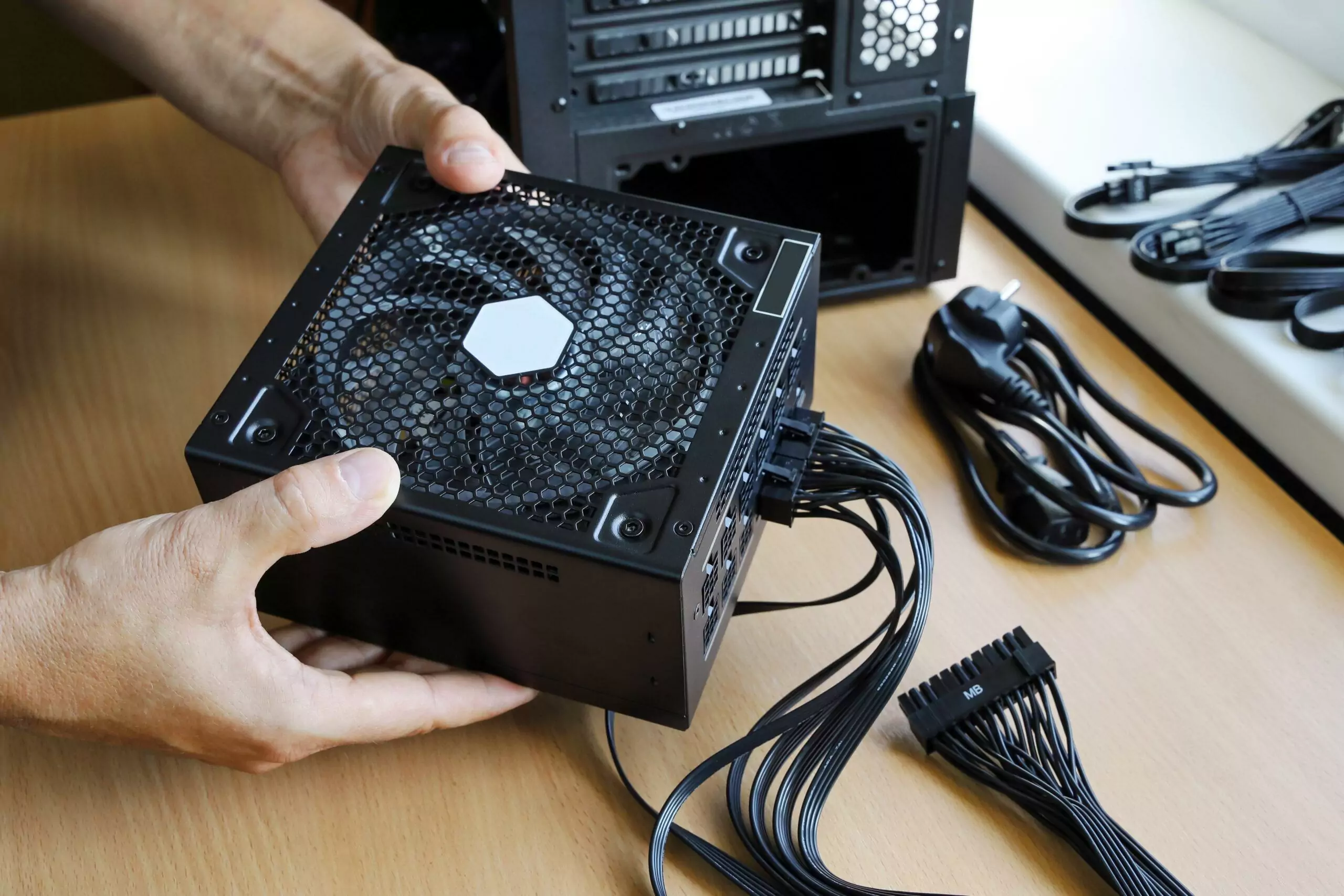Hands hold power supply unit with connected wires to install it in computer case