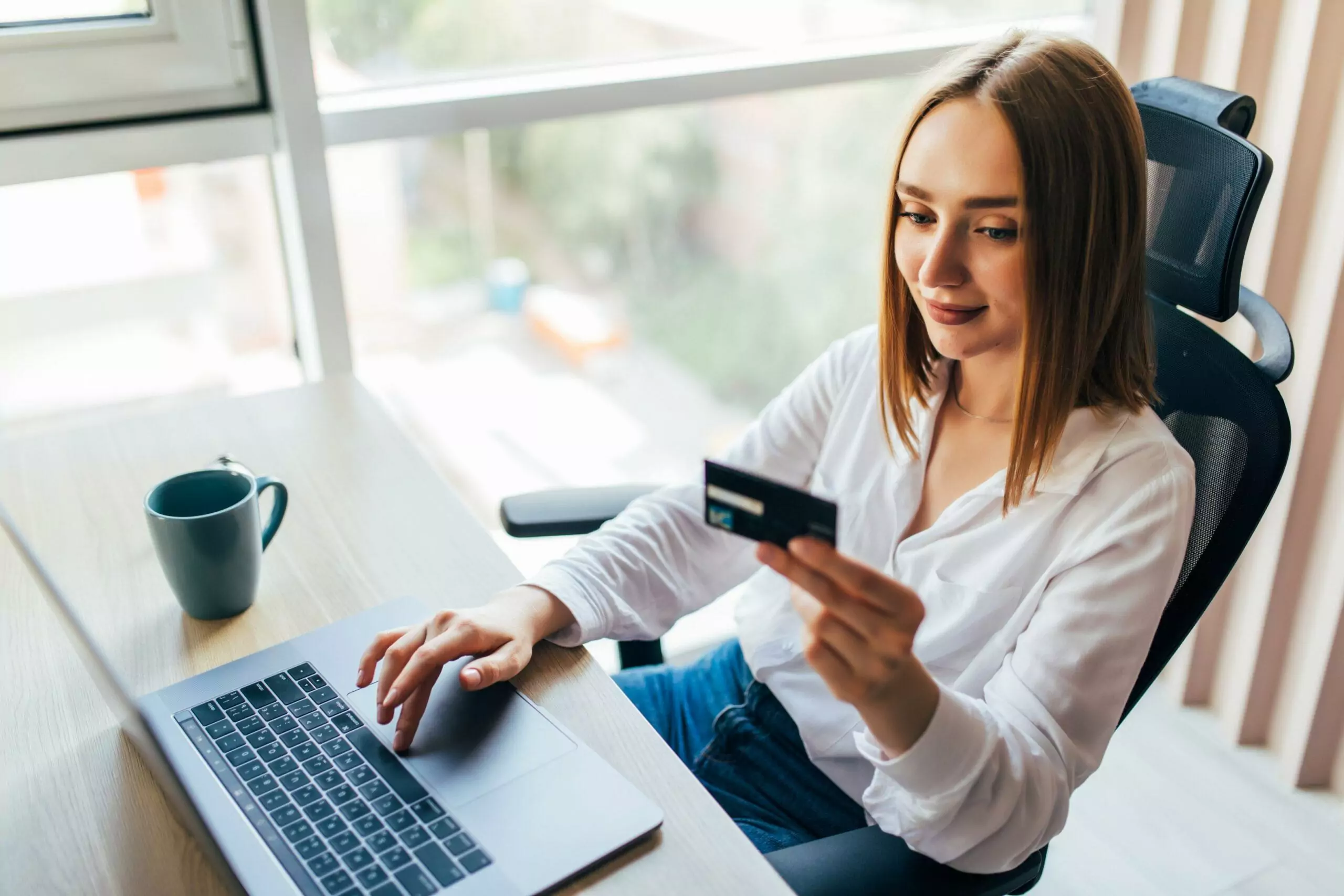 Portrait of a girl with shoulder-length sleek hair holding credit card and using laptop