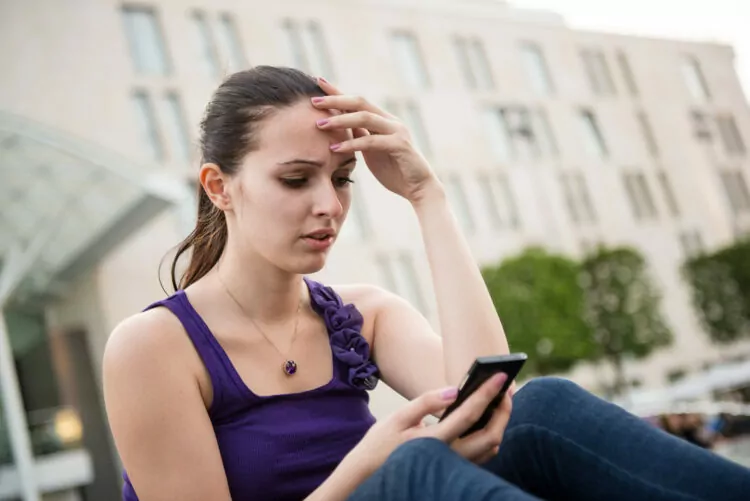 young woman looking worried outdoor using her phone