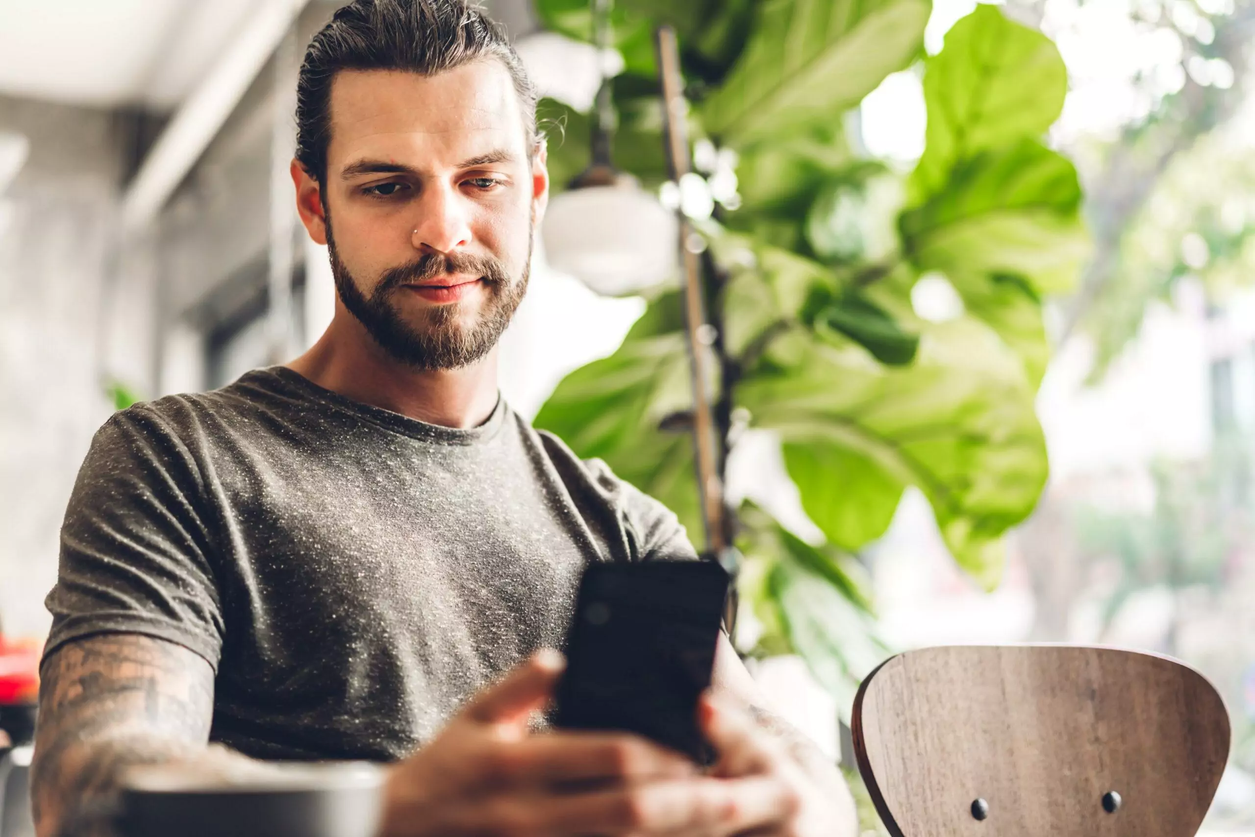 Handsome bearded hipster man using smartphone with coffee at table