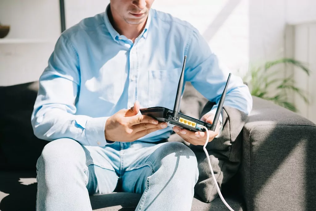 Businessman sitting on sofa and holding plugged router.
