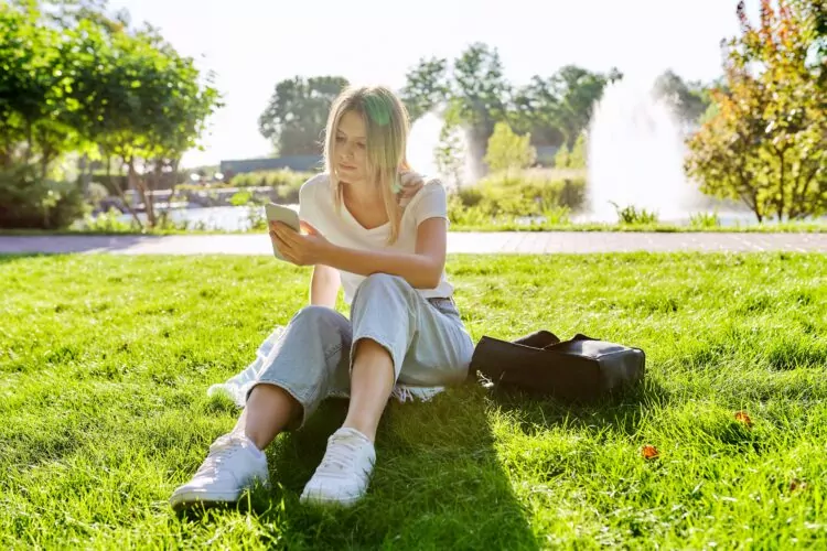 Sad young woman sitting alone in the park with smartphone