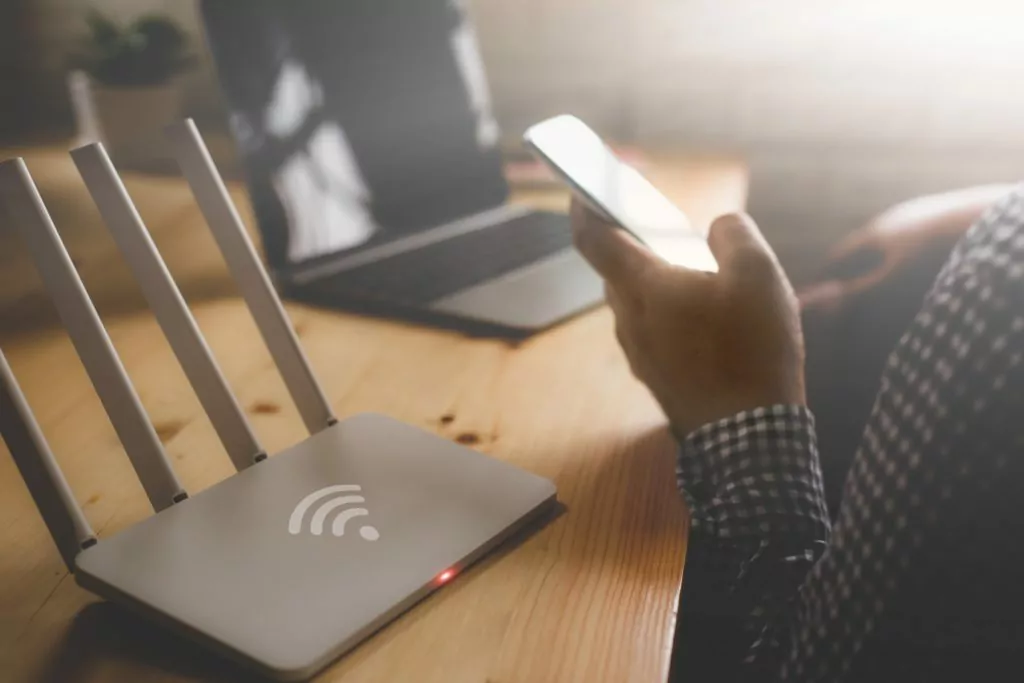 Close-up of a wireless router with a man using his smartphone and laptop.