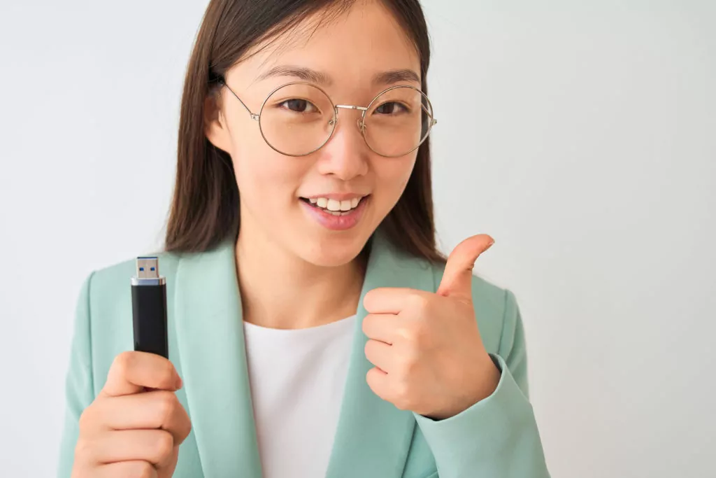 Young woman with USB flash drive, doing a thumbs up sign with her hand.